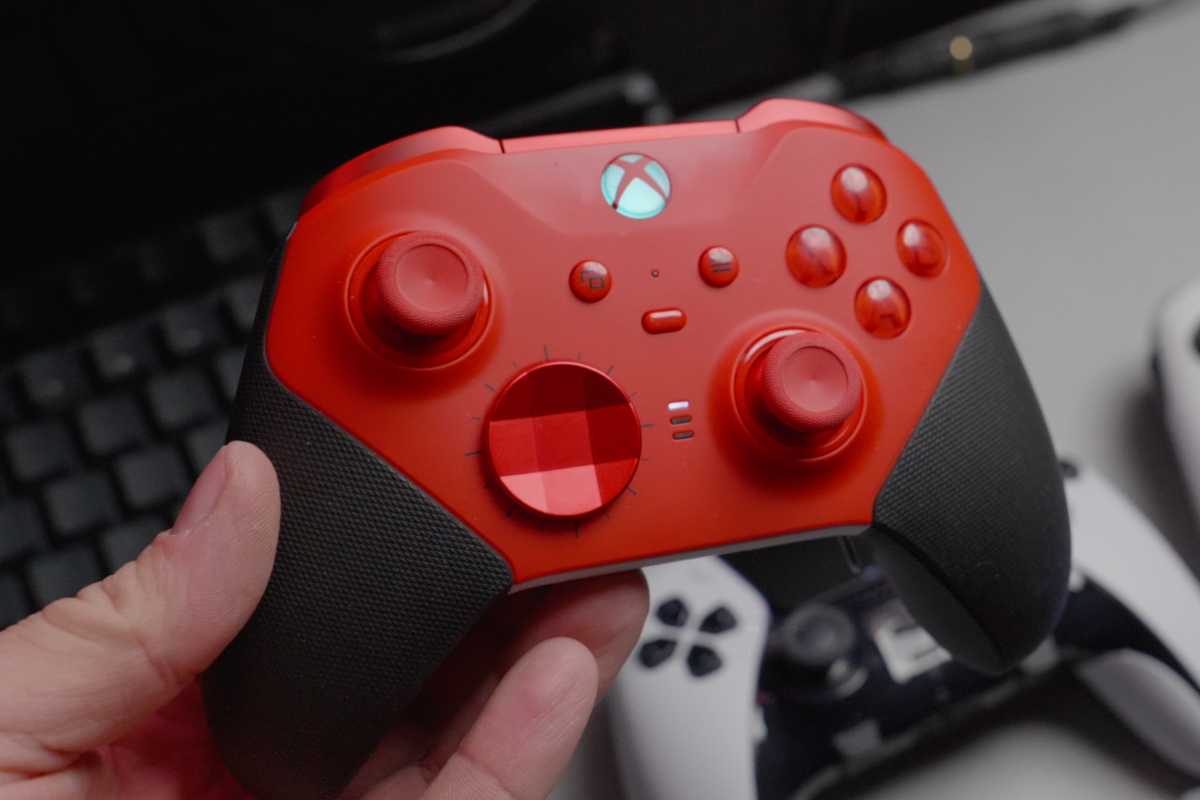 Red wireless Xbox gaming controller in hand held over desk alternate view