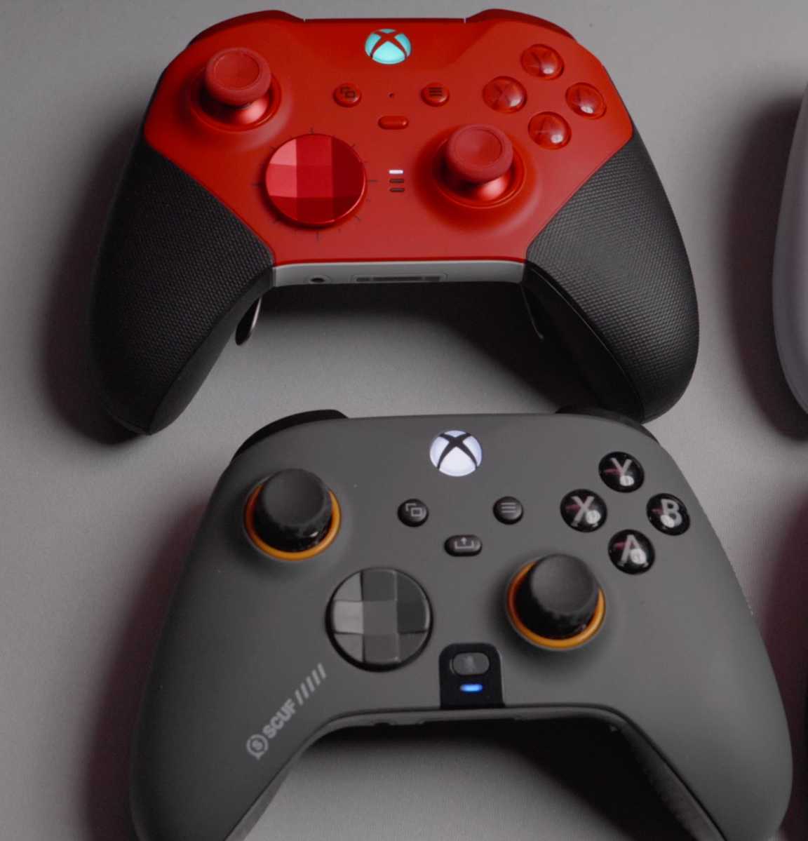 Red wireless Xbox gaming controller next to gray Scuf gaming controller