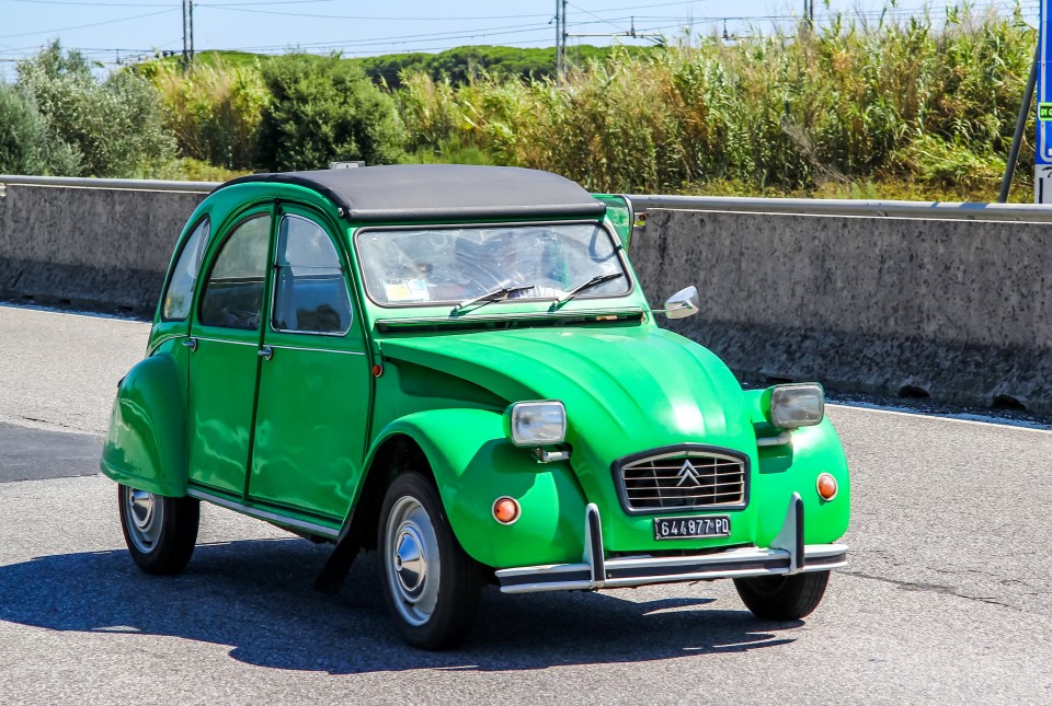 Green Citroën 2CV driving on a road.