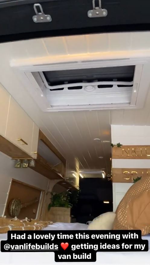 Interior of a converted van with a bed, overhead cabinets, and a roof vent.