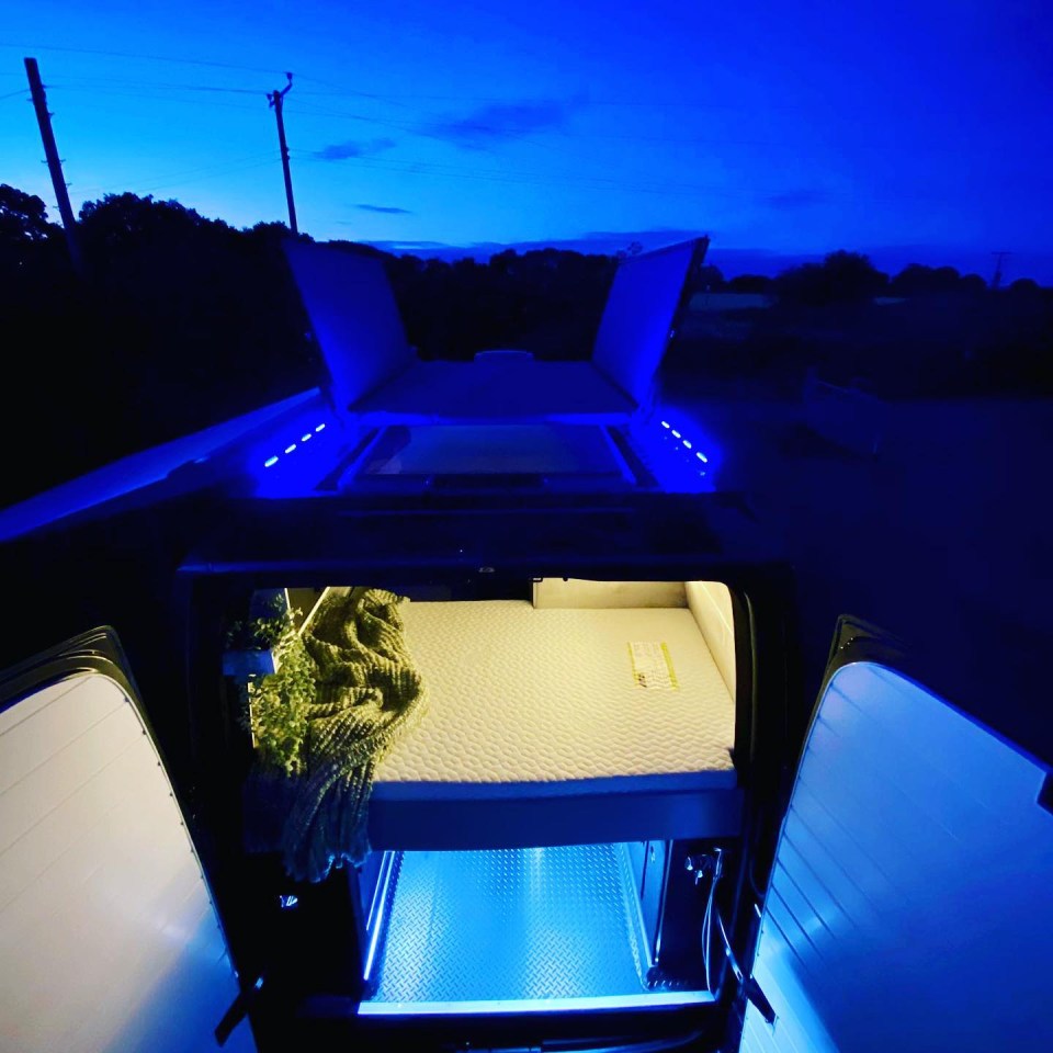 Interior of a custom-built van at night, showing a bed and blue LED lights.