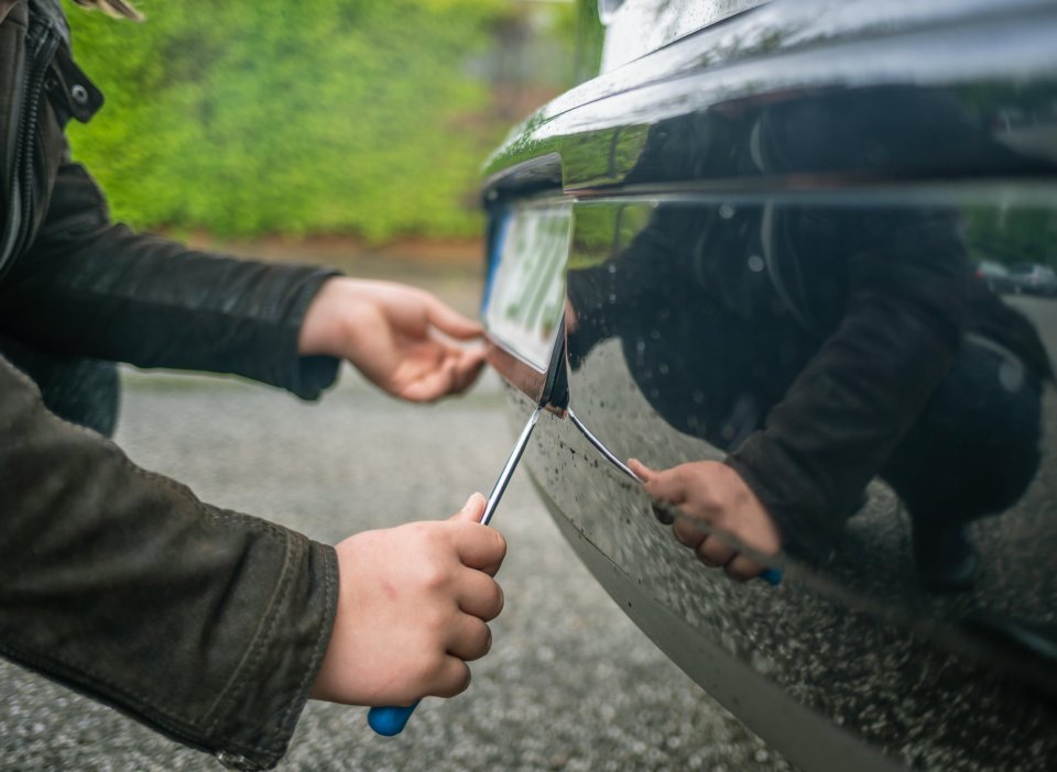 Person stealing a license plate from a car with a screwdriver.