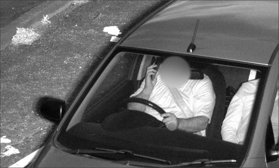 Black and white image of a driver using a mobile phone while driving.