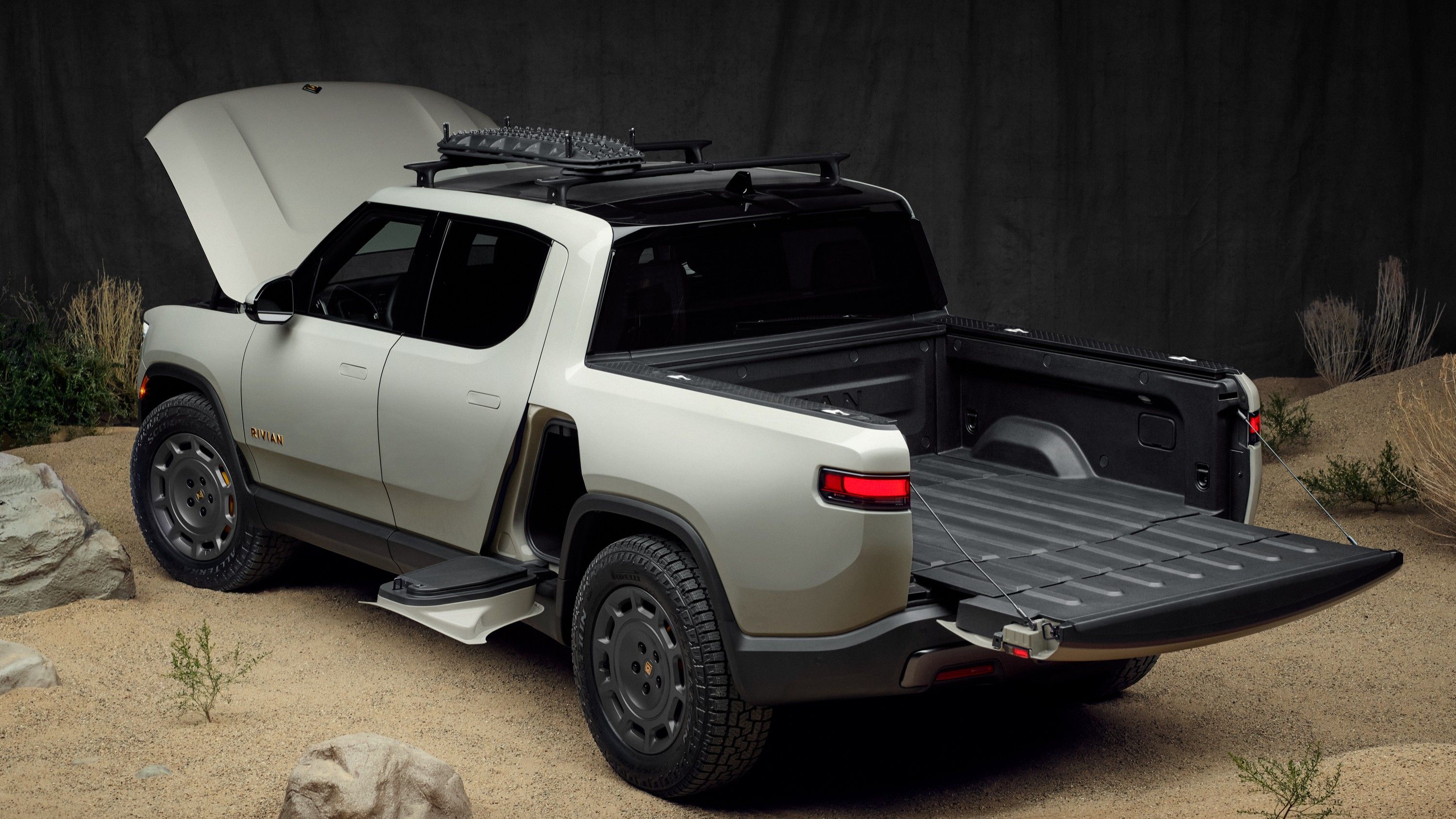 Exterior rear three-quarters static photo of a gray 2025 Rivian R1T California Dune Edition with the frunk and tailgate open