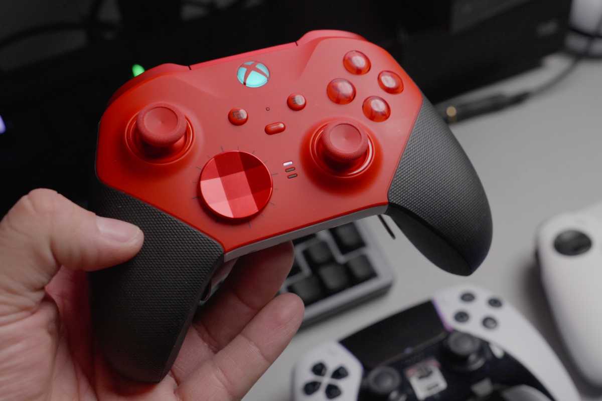 Red wireless Xbox gaming controller in hand held over desk