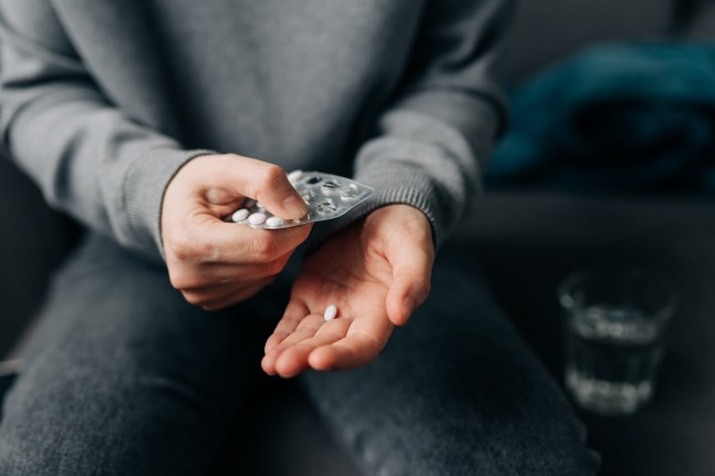 A person holding out a pill and taking a pill from the pill container.