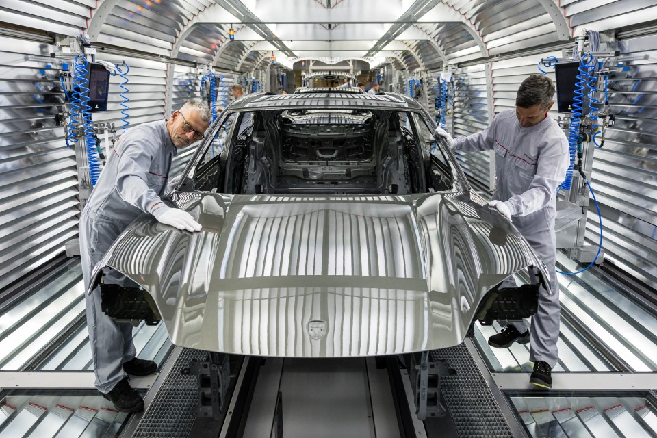 Workers assembling an electric Porsche Macan at a factory.