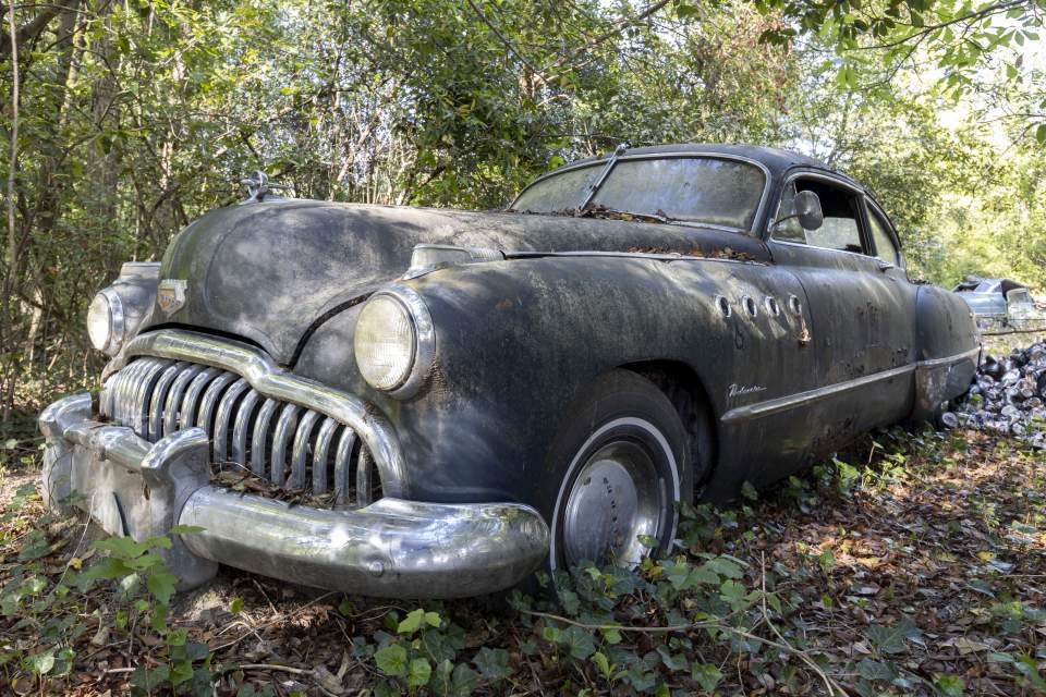 Overgrown, abandoned Buick Roadmaster in woods.