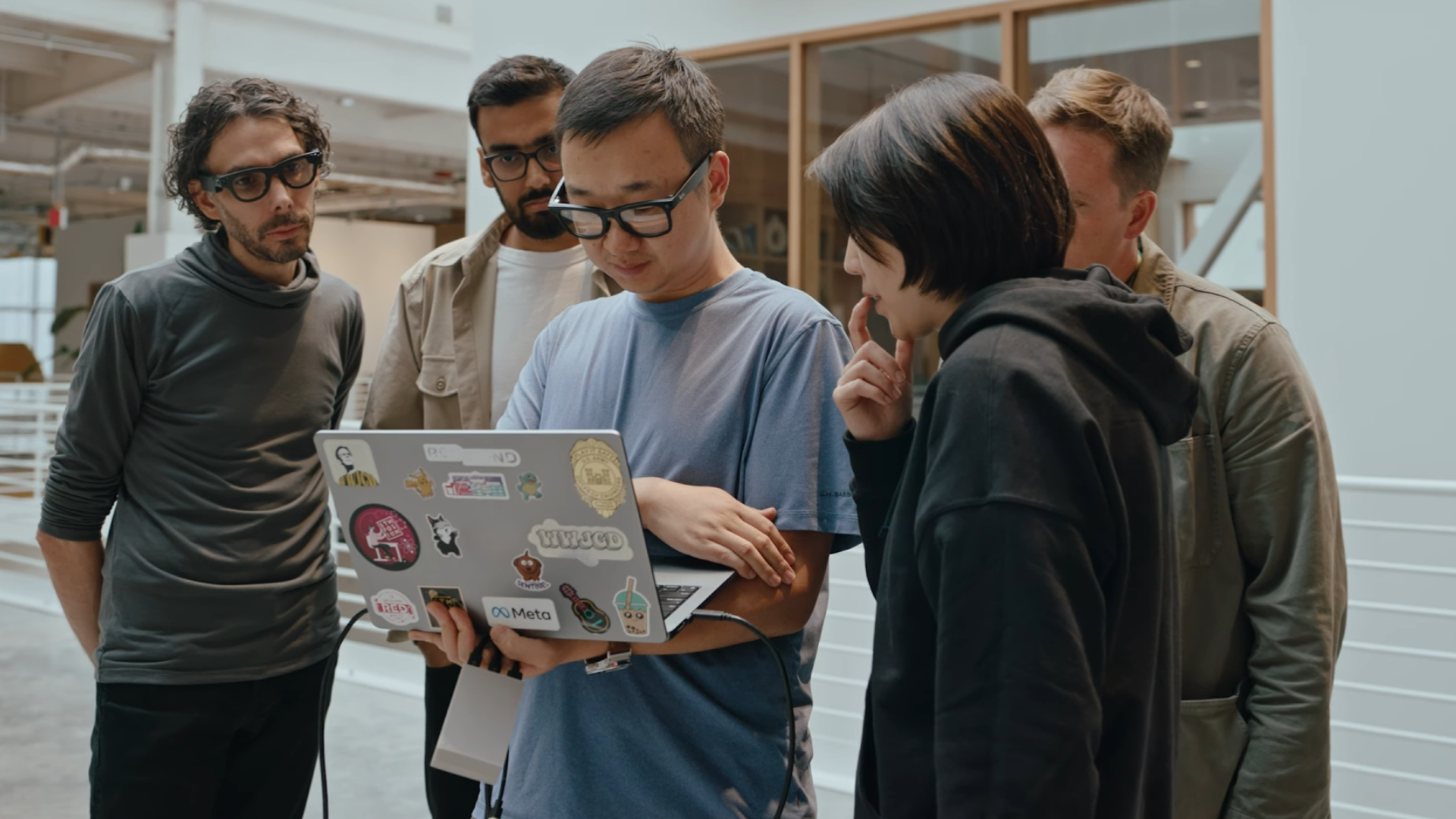 People wearing the Meta Aria Gen 2 glasses while stood around a laptop