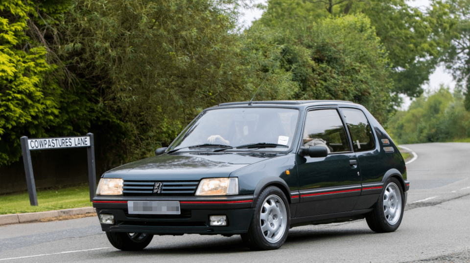 Dark green Peugeot 106 driving down a road.