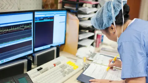 Getty Images A nurse fills in a form in front of screens