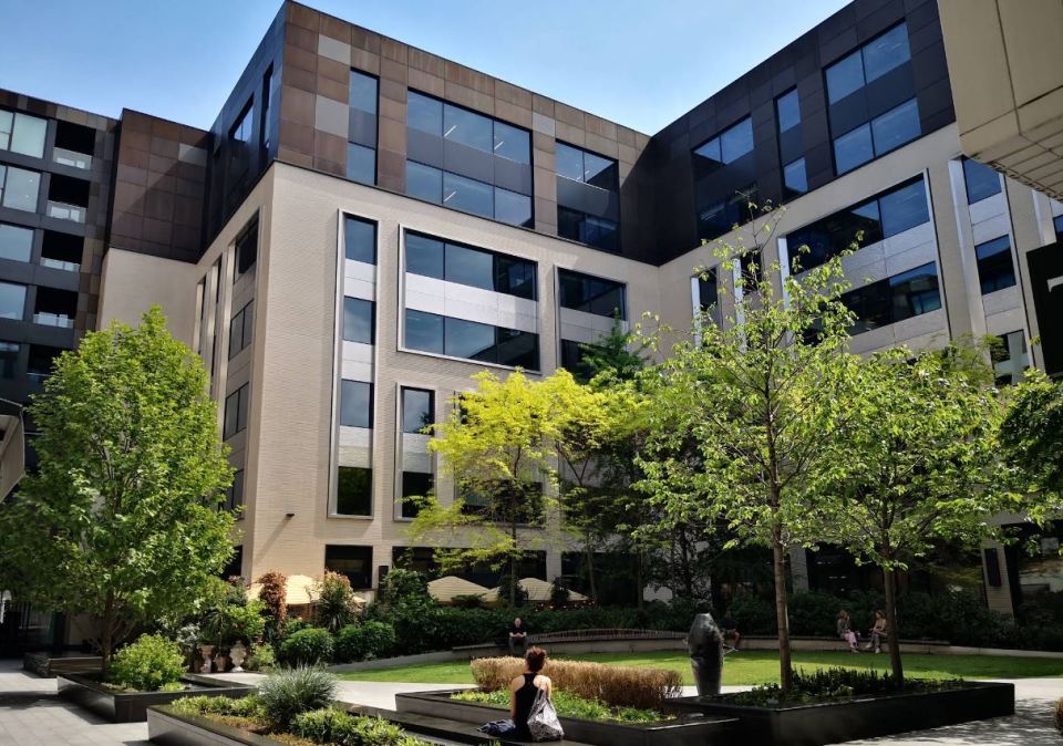 Modern office building courtyard with landscaping and people sitting.